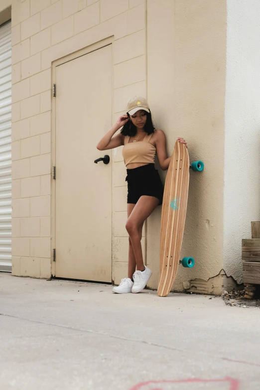 a woman leaning against a wall with a skateboard, by Robbie Trevino, croptop and shorts, brown and cyan color scheme, cindy avelino, upper body image