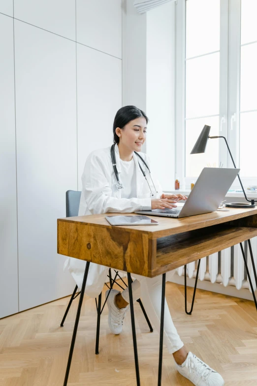 a woman sitting at a desk using a laptop computer, by Julia Pishtar, white coat, wooden, asian human, ultrawide image