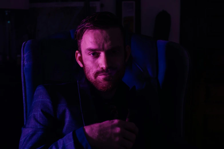 a man sitting in a chair looking at his cell phone, a character portrait, inspired by Niko Henrichon, pexels contest winner, blue and purple lighting, pewdiepie, dark suit, calm night. over shoulder shot