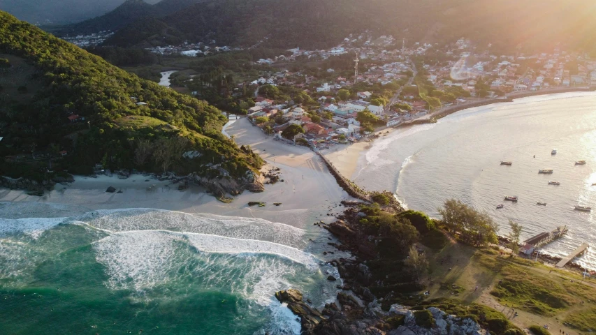 a large body of water next to a lush green hillside, by Lucas Vorsterman, pexels contest winner, which shows a beach at sunset, location ( favela ), aerial footage, white beaches