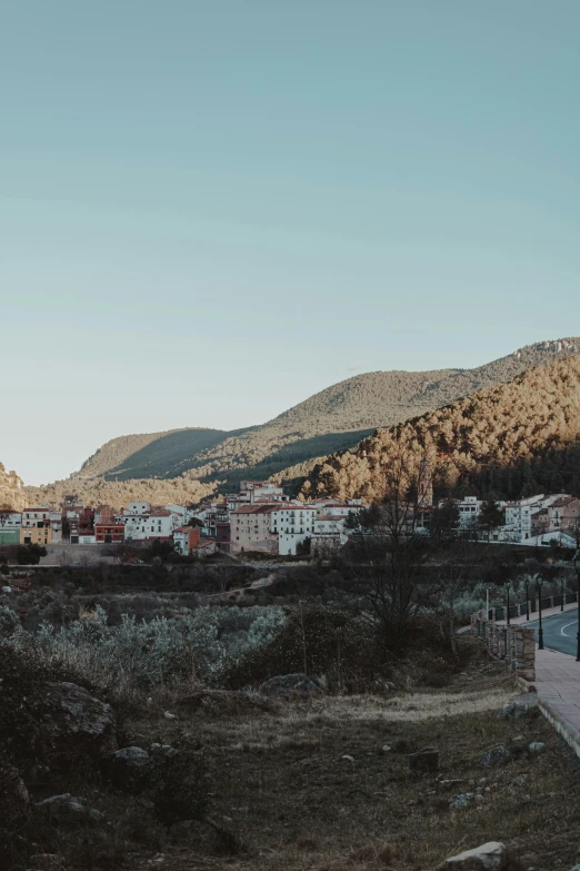 a train traveling down a train track next to a lush green hillside, trending on unsplash, les nabis, realistic photo of a town, in spain, twilight ; wide shot, sunfaded