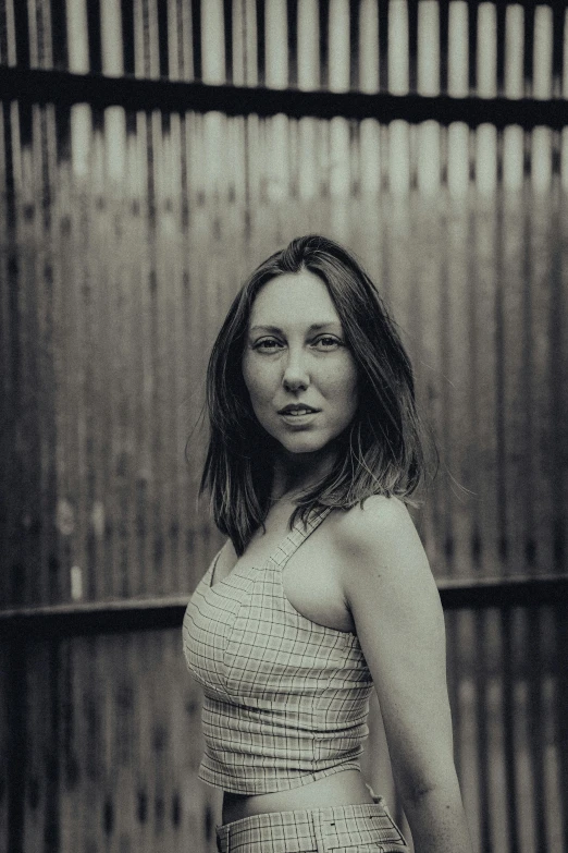 a woman standing in front of a wooden fence, a black and white photo, by Andrew Stevovich, carice van houten, portrait image, cardboard, promo image