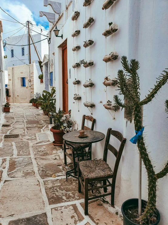 a narrow cobblestone street with tables and chairs, by Alexis Grimou, cycladic sculptural style, wrapped in cables and flowers, dominant wihte and blue colours, unsplash photography