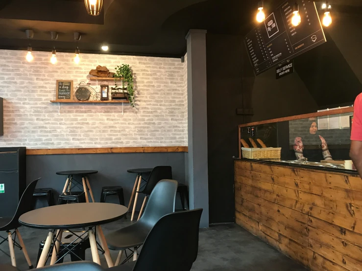 a man standing in front of a counter in a restaurant, by Emma Andijewska, unsplash, private press, background image, grey and dark theme, an escape room in a small, cold brew coffee )