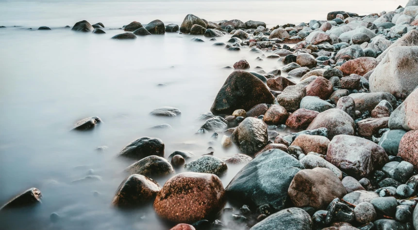 a rocky beach next to a body of water, by Jesper Knudsen, smooth round shapes, beautiful random images, faded colors, brown