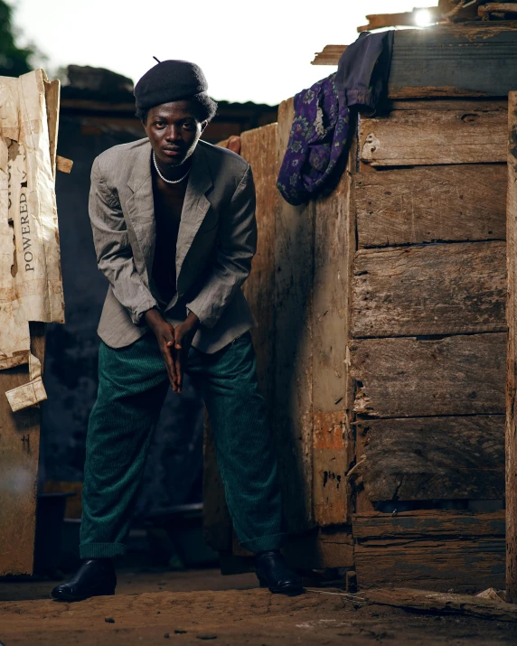 a man standing next to a pile of boxes, an album cover, by Elsa Bleda, trending on unsplash, afrofuturism, young male with walking stick, confident pose, in africa, squatting