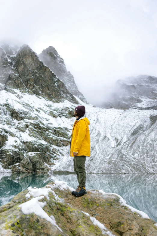 a man standing on top of a snow covered mountain, inspired by national geographic, pexels contest winner, wearing a yellow hoodie, standing next to water, avatar image, chamonix