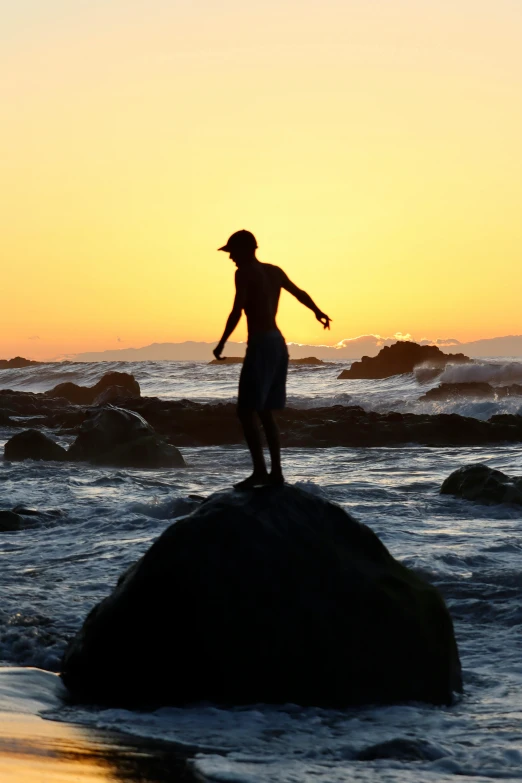 a man standing on top of a rock in the ocean, by Arie Smit, sunset beach, teenage boy, south african coast, silhouette :7