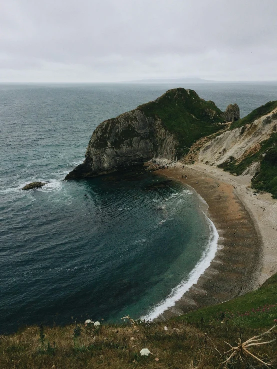 a large body of water sitting on top of a lush green hillside, an album cover, pexels contest winner, beautiful dark beach landscape, victorian arcs of sand, today\'s featured photograph 4k, gloomy weather