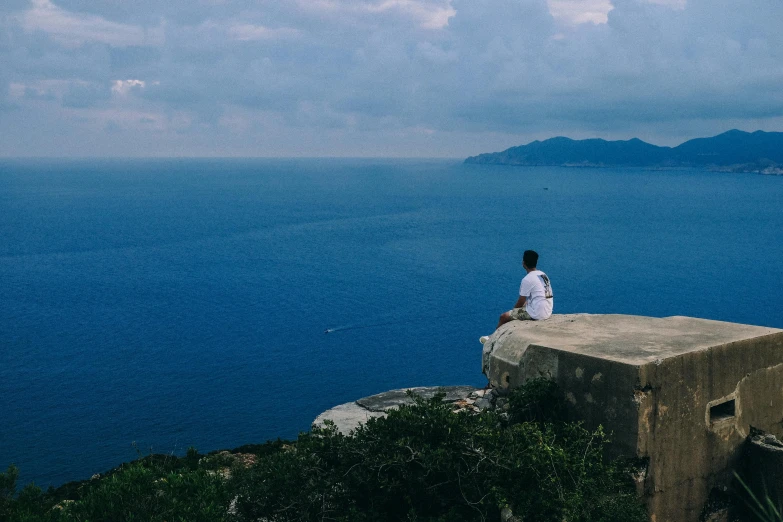 a man sitting on top of a rock next to the ocean, pexels contest winner, mediterranean vista, lo fi, panoramic shot, fan favorite