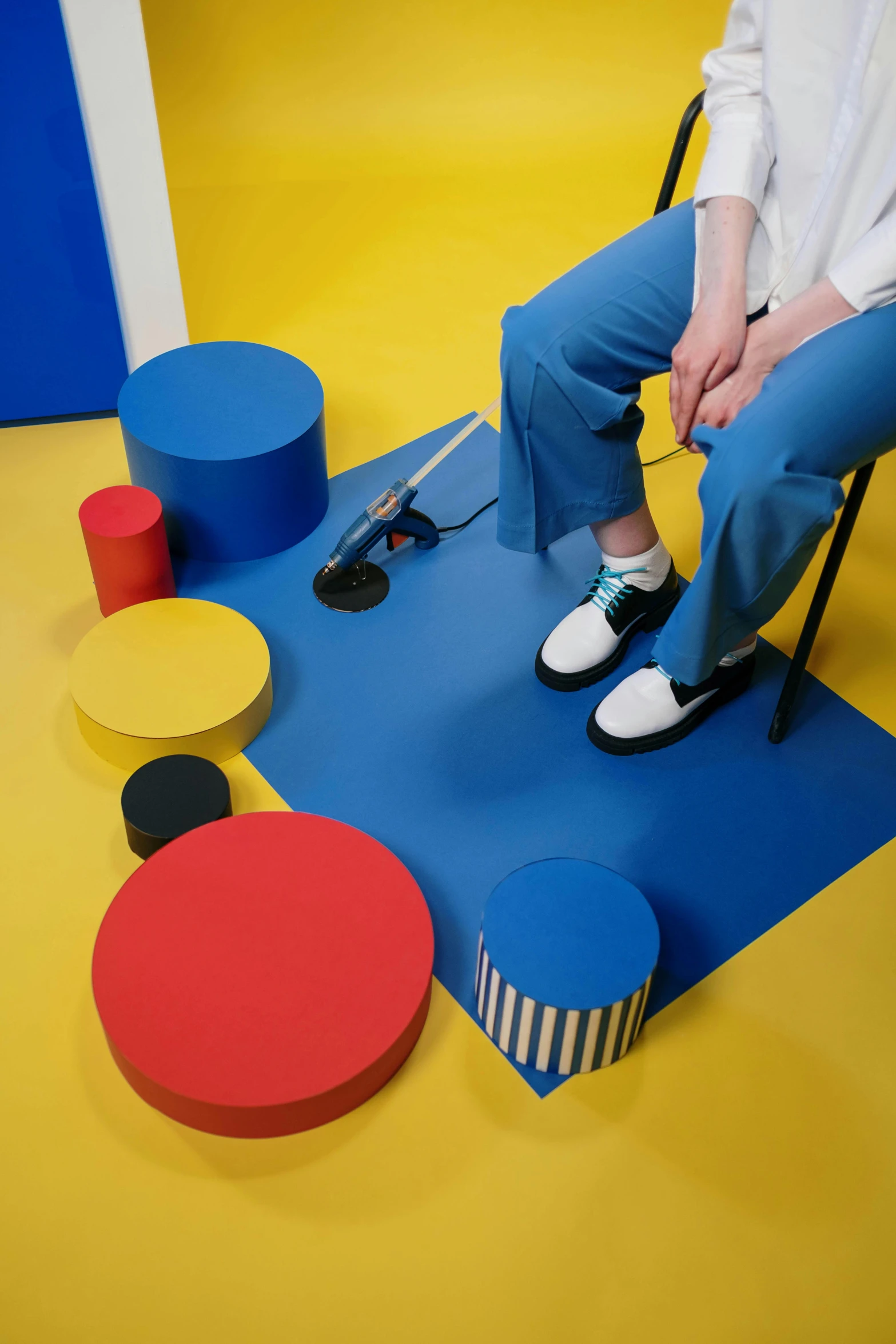 a woman sitting in a chair in a brightly colored room, an album cover, inspired by Bauhaus, trending on unsplash, de stijl, sneakers, blue pants, studio floor, dezeen showroom