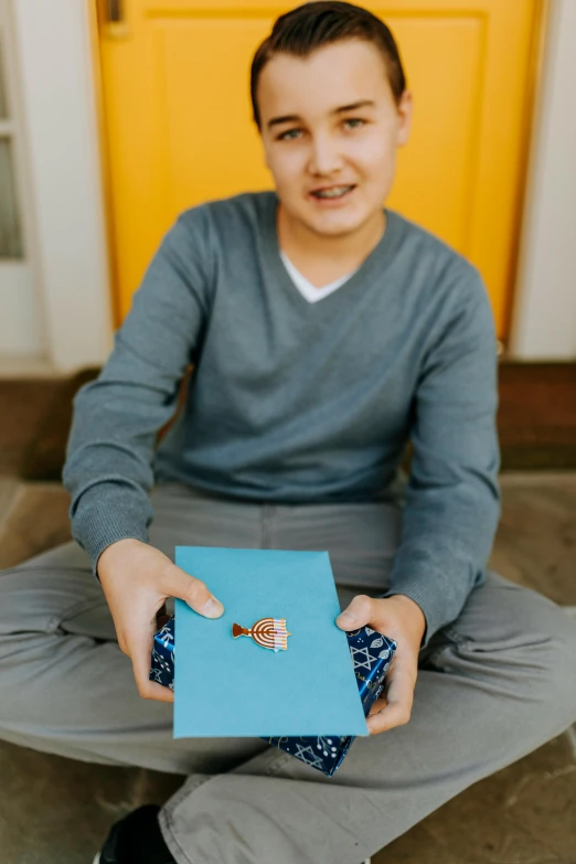 a man sitting in front of a yellow door holding a book, sapphire butterfly jewellery, teen boy, wearing a light blue shirt, holding a squid