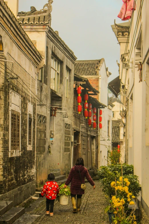 a woman and a child walking down a cobblestone street, a silk screen, inspired by Cui Bai, pexels contest winner, red flowers, zhouzhuang ancient town, white buildings, late afternoon