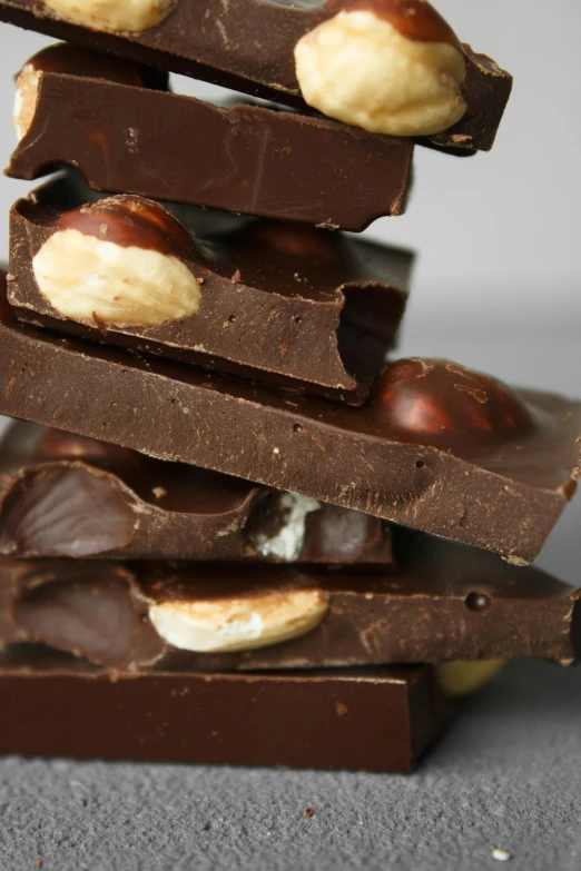 a stack of pieces of chocolate with nuts on top, by Jessie Algie, on a gray background, zoomed in, thumbnail