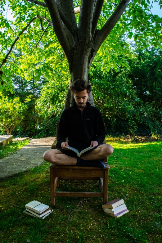 a man sitting in a chair reading a book, permaculture, young greek man, mind bending, 2019 trending photo