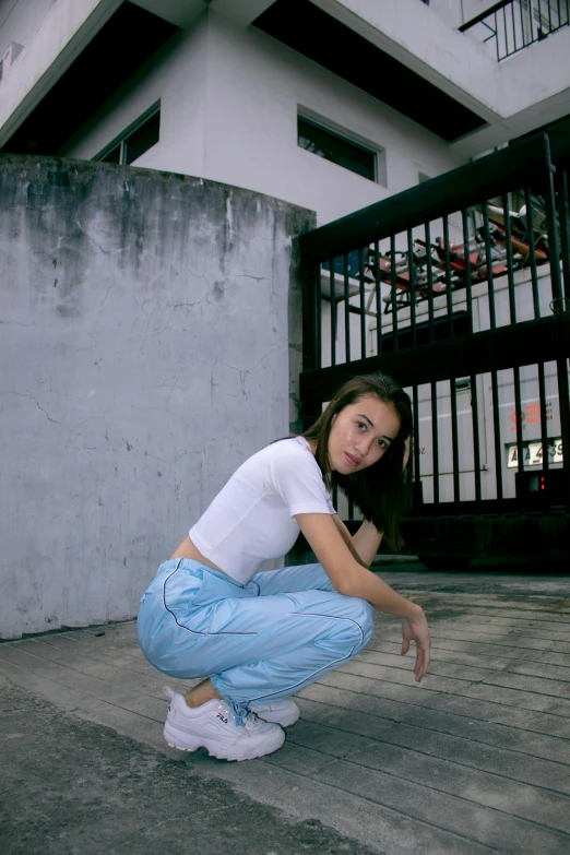 a woman squatting down in front of a building, an album cover, inspired by Leng Mei, unsplash, blue pants, low quality photo, satisfied pose, croptop