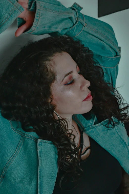a beautiful young woman laying on top of a bed, an album cover, inspired by Elsa Bleda, trending on pexels, renaissance, jean jacket, liberty curls, dark teal, official music video