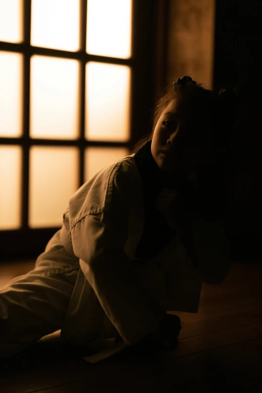 a woman sitting on the floor in front of a window, a picture, inspired by Goyō Hashiguchi, unsplash, dramatic backlighting, girl with plaits, aikido, nighttime