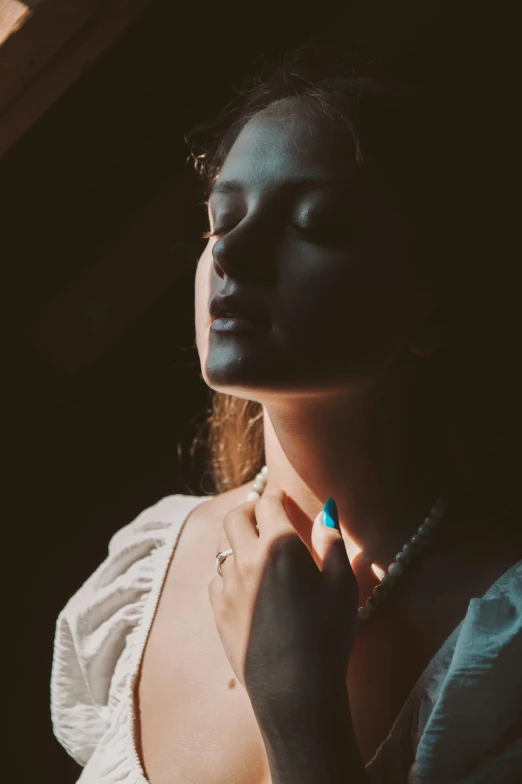 a woman in a white dress standing next to a window, inspired by Elsa Bleda, trending on pexels, renaissance, neck zoomed in from lips down, portrait of a lady vampire, jewelry, in a sunbeam