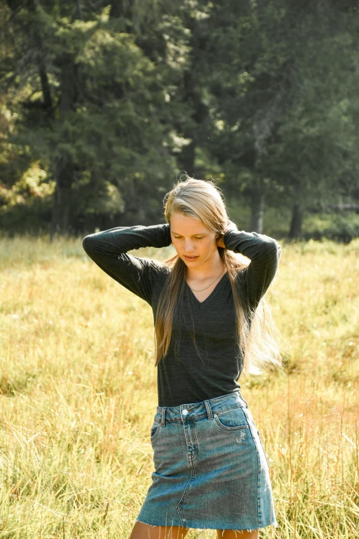 a woman standing in a field with her hands on her head, wearing a dark shirt and jeans, sydney hanson, profile image, avatar image