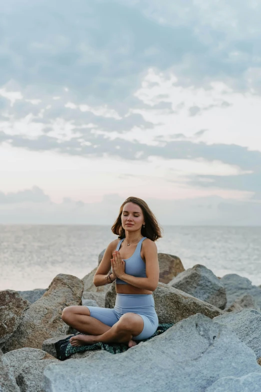 a woman sitting on top of a rock next to the ocean, anjali mudra, calmly conversing 8k, sofya emelenko, 6 : 3 0 am