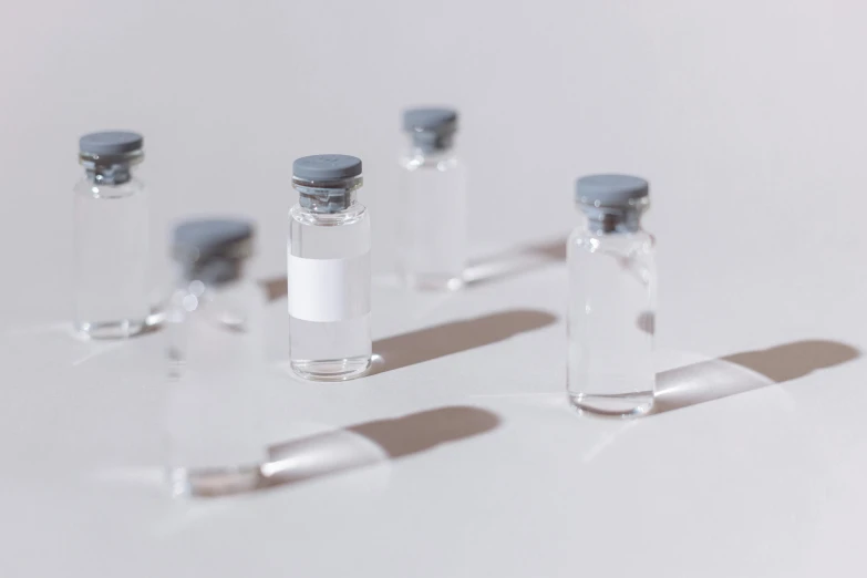 a group of vials sitting on top of a table, trending on pexels, on a pale background, detailed white liquid, hgh, grey