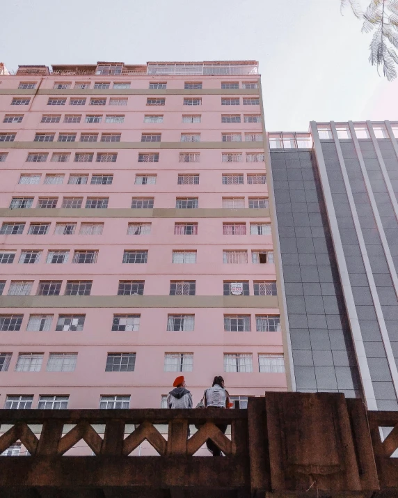 a couple of people that are standing on a bridge, a cartoon, unsplash, quito school, pink marble building, high rises, south jakarta, low quality photo