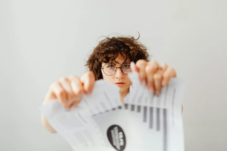 a woman holding a bunch of papers in front of her face, pexels contest winner, rebecca sugar, girl with glasses, charts, avatar image