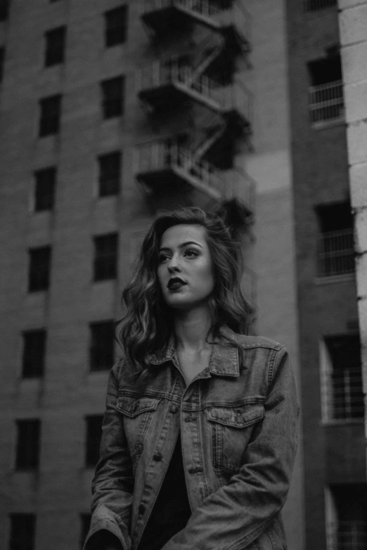 a woman standing in front of a tall building, a black and white photo, inspired by Elsa Bleda, unsplash contest winner, realism, pout, she wears a jacket, cynthwave, 2 4 year old female model