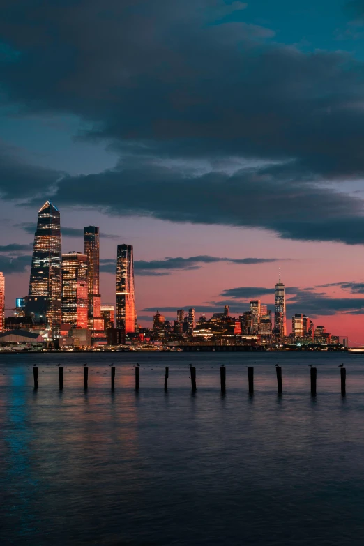 a large body of water with a city in the background, unsplash contest winner, hudson river school, humid evening, tall metal towers, red glow in sky, new jersey