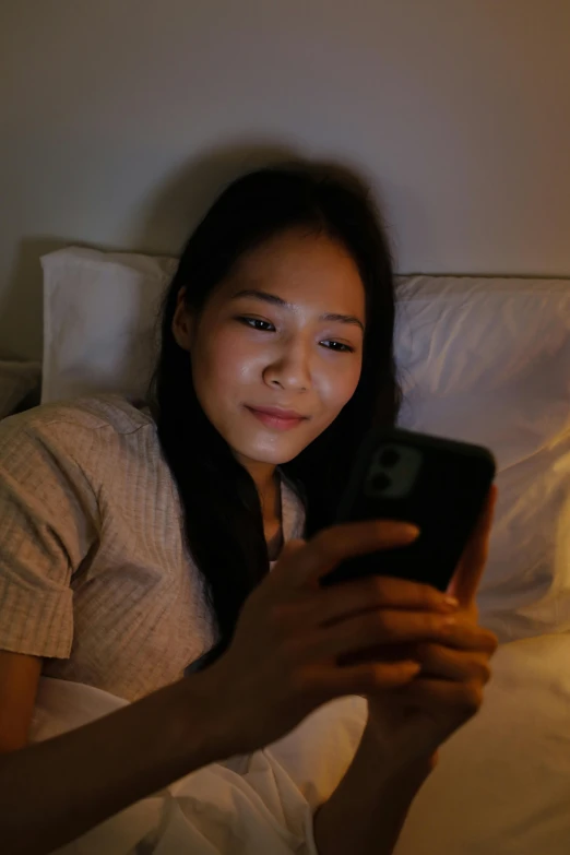 a woman laying in bed looking at her cell phone, a picture, trending on pexels, south east asian with round face, nightlight, twitch streamer, slightly round chin