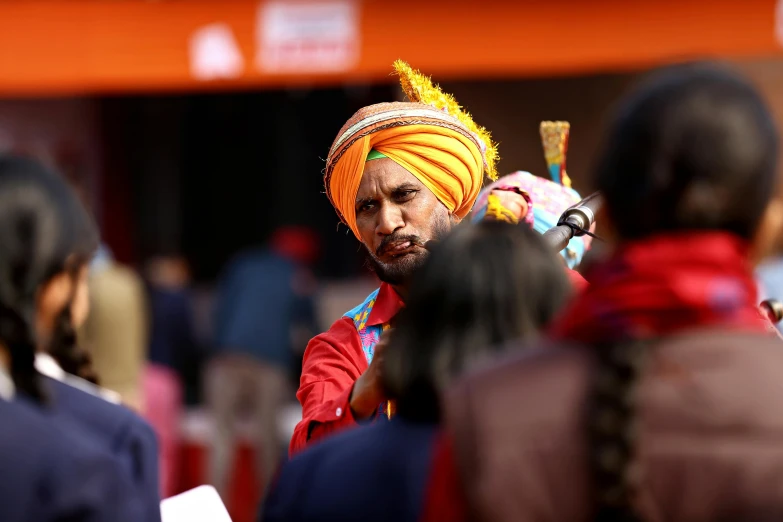 a man in a turban is talking to a group of people, by Manjit Bawa, pexels contest winner, samikshavad, square, orange extremely coherent, red cloth around his shoulders, man holding spear