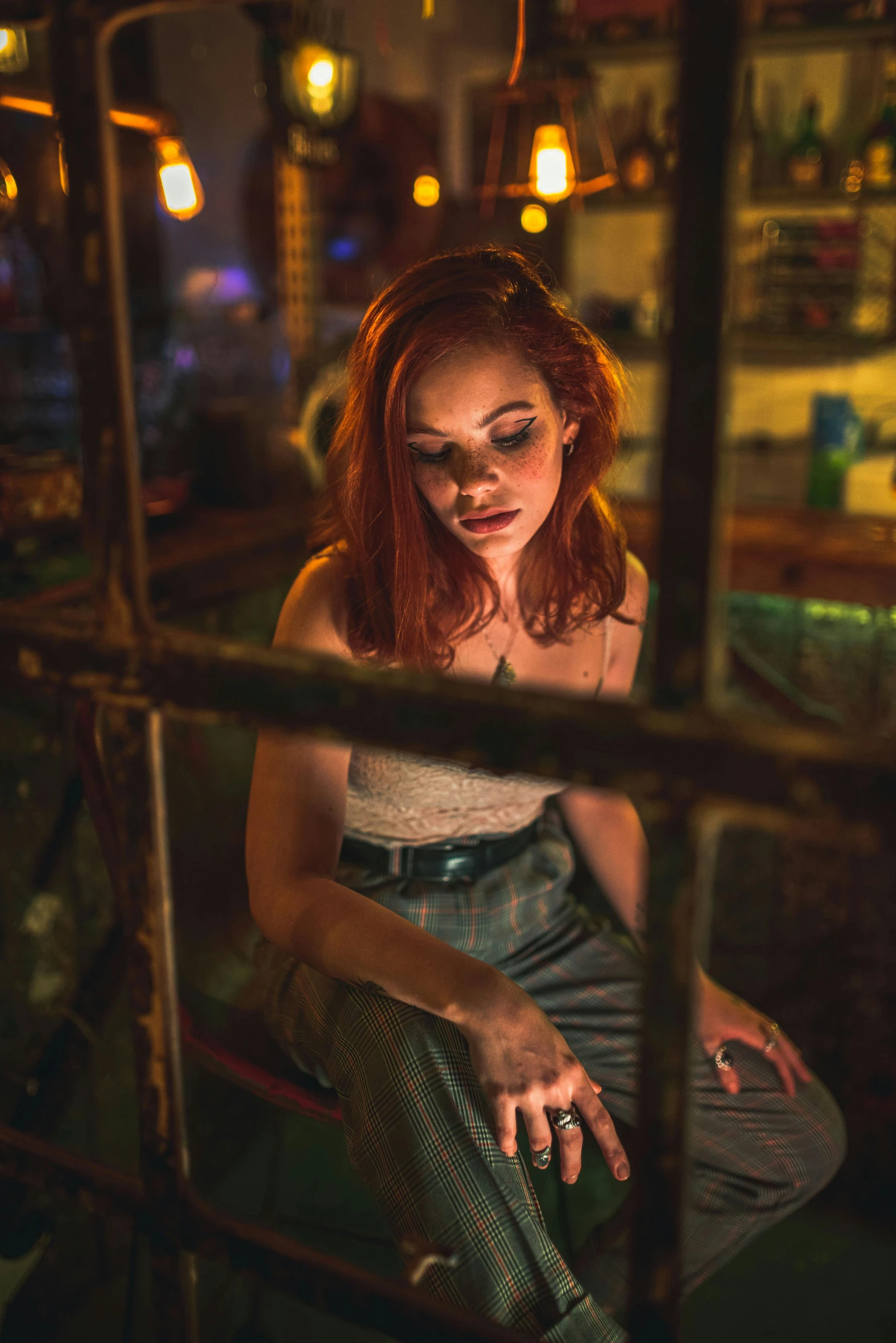 a woman sitting on a chair in front of a window, a portrait, inspired by Elsa Bleda, trending on pexels, dimly lit dive bar, ( redhead, vanessa morgan, girl under lantern