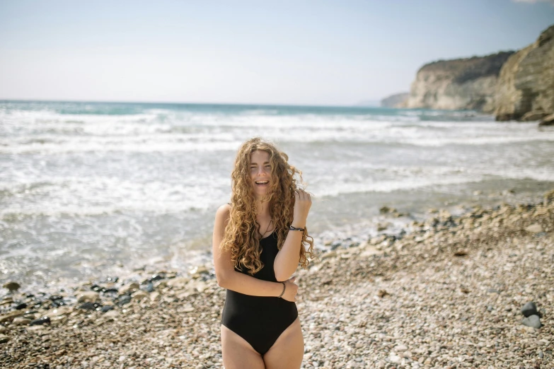 a woman standing on a beach next to the ocean, a portrait, pexels contest winner, renaissance, cute girl wearing tank suit, avatar image, cyprus, with long curly hair