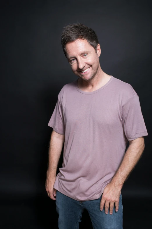 a man standing in front of a black background, an album cover, inspired by Adam Pijnacker, wearing purple undershirt, simon stalberg, grey backdrop, wearing pajamas