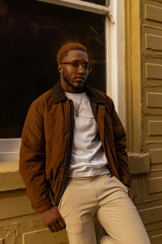 a man leaning against a wall in front of a window, an album cover, inspired by Barthélemy Menn, trending on pexels, brown clothes, wearing gold glasses, wearing a turtleneck and jacket, teddy fresh