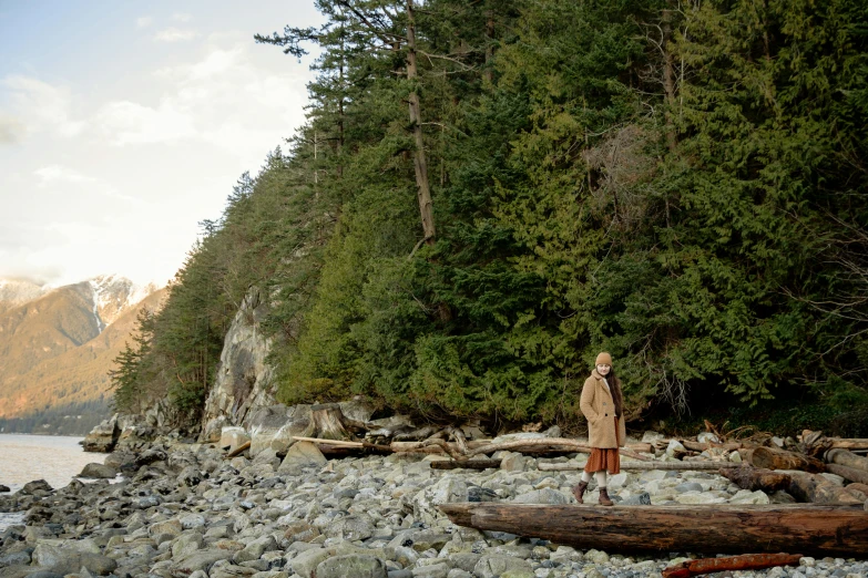 a man standing on a rocky beach next to a body of water, endor forest, brown robes, vancouver, conde nast traveler photo