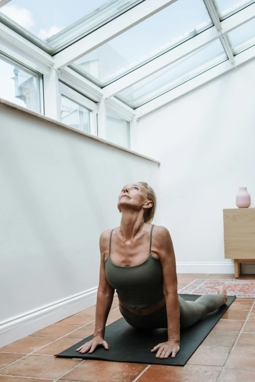 a woman sitting on a yoga mat in a room, by Rachel Reckitt, looking upwards, profile image, stretching to walls, studio photo