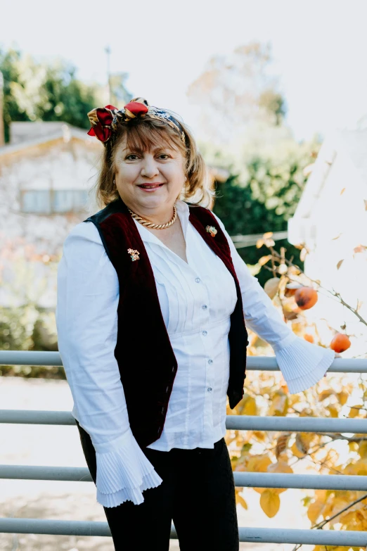 a woman standing next to a fence with an apple tree in the background, wearing authentic attire, professional profile picture, vests and corsets, wearing festive clothing