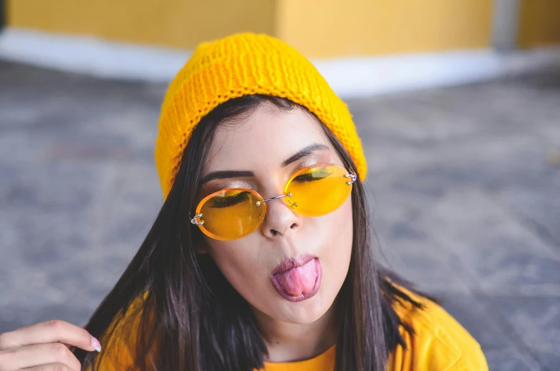a woman sticking her tongue out while wearing sunglasses, trending on pexels, pop art, yellow cap, college girls, colors: yellow, smooggy