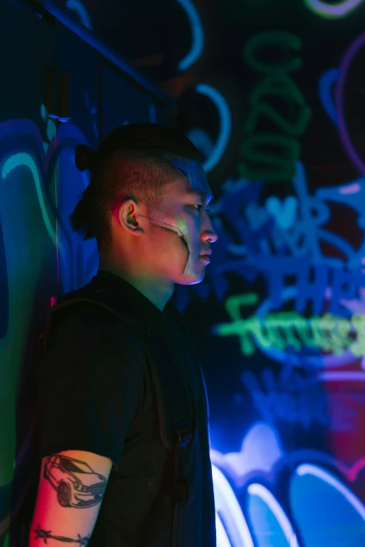 a man standing in front of a wall covered in graffiti, inspired by Liam Wong, unsplash, backlit ears, unreal engine : : rave makeup, asian human, bisexual lighting