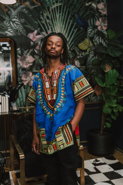 a man standing in front of a black and white checkered floor, an album cover, inspired by Ras Akyem, trending on unsplash, renaissance, blue tunic and robes, wearing an african dress, prideful, thumbnail