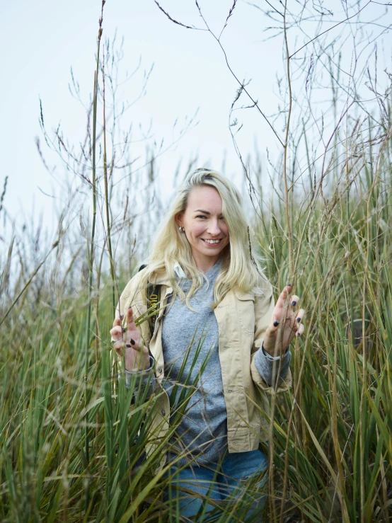 a woman standing in a field of tall grass, a portrait, unsplash, happening, wearing farm clothes, a blond, on the coast, while smiling for a photograph