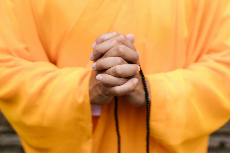 a close up of a person holding a rosary, unsplash, orange robe, buddhist monk, yellow, 15081959 21121991 01012000 4k