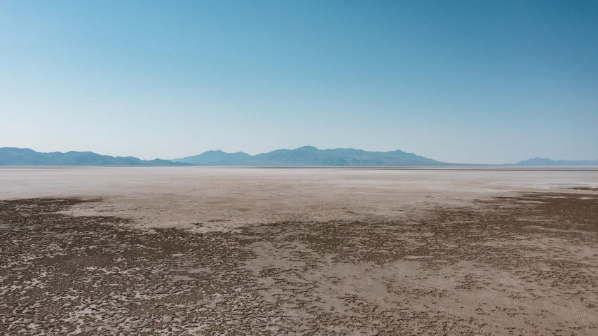 a desert landscape with mountains in the distance, unsplash contest winner, land art, cloudless sky, salt flats with scattered ruins, beach landscape, background image