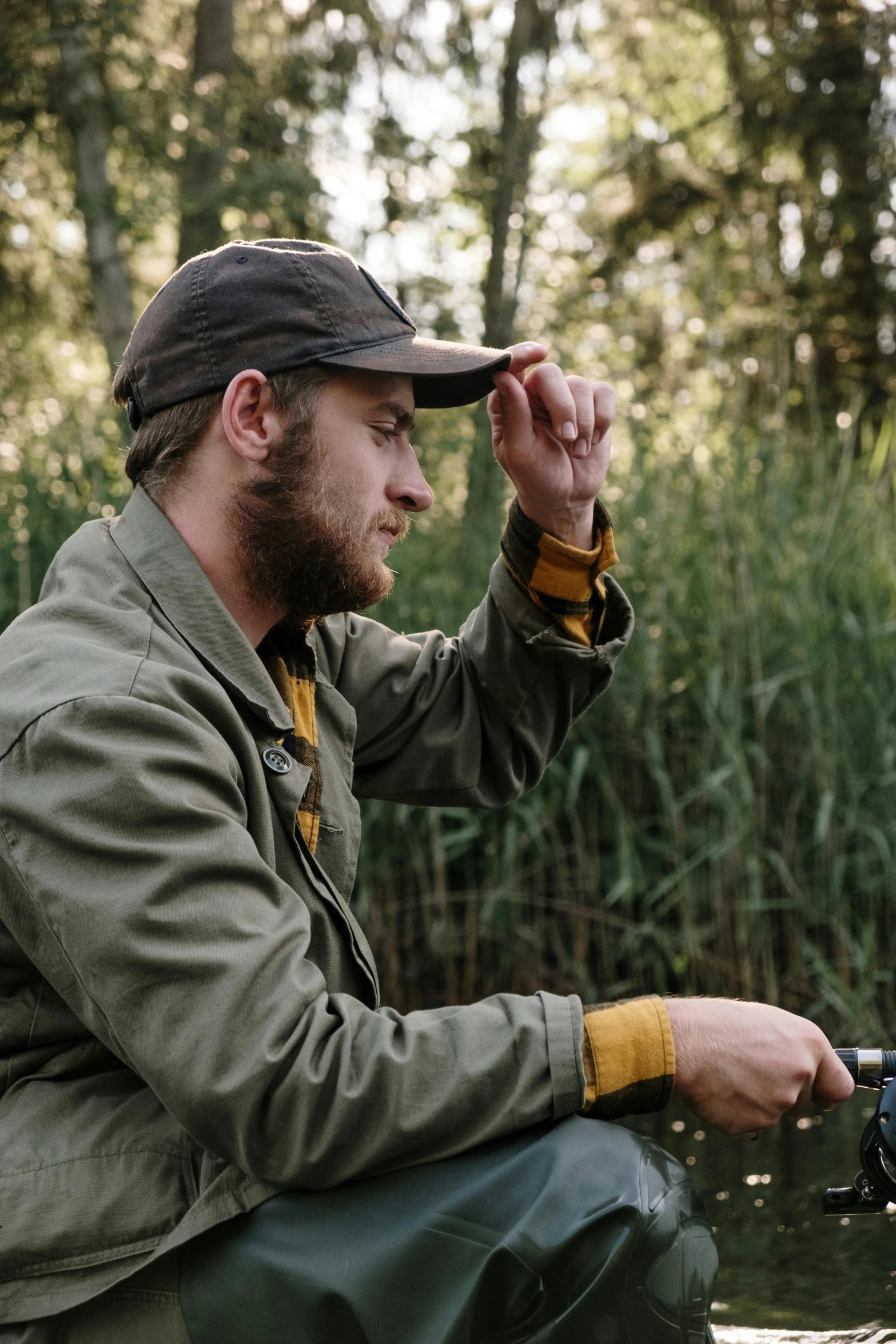 a man sitting on top of a boat holding a fish, by Jan Tengnagel, unsplash, wearing hunter coat, near pond, picture of a male biker, concentrated look
