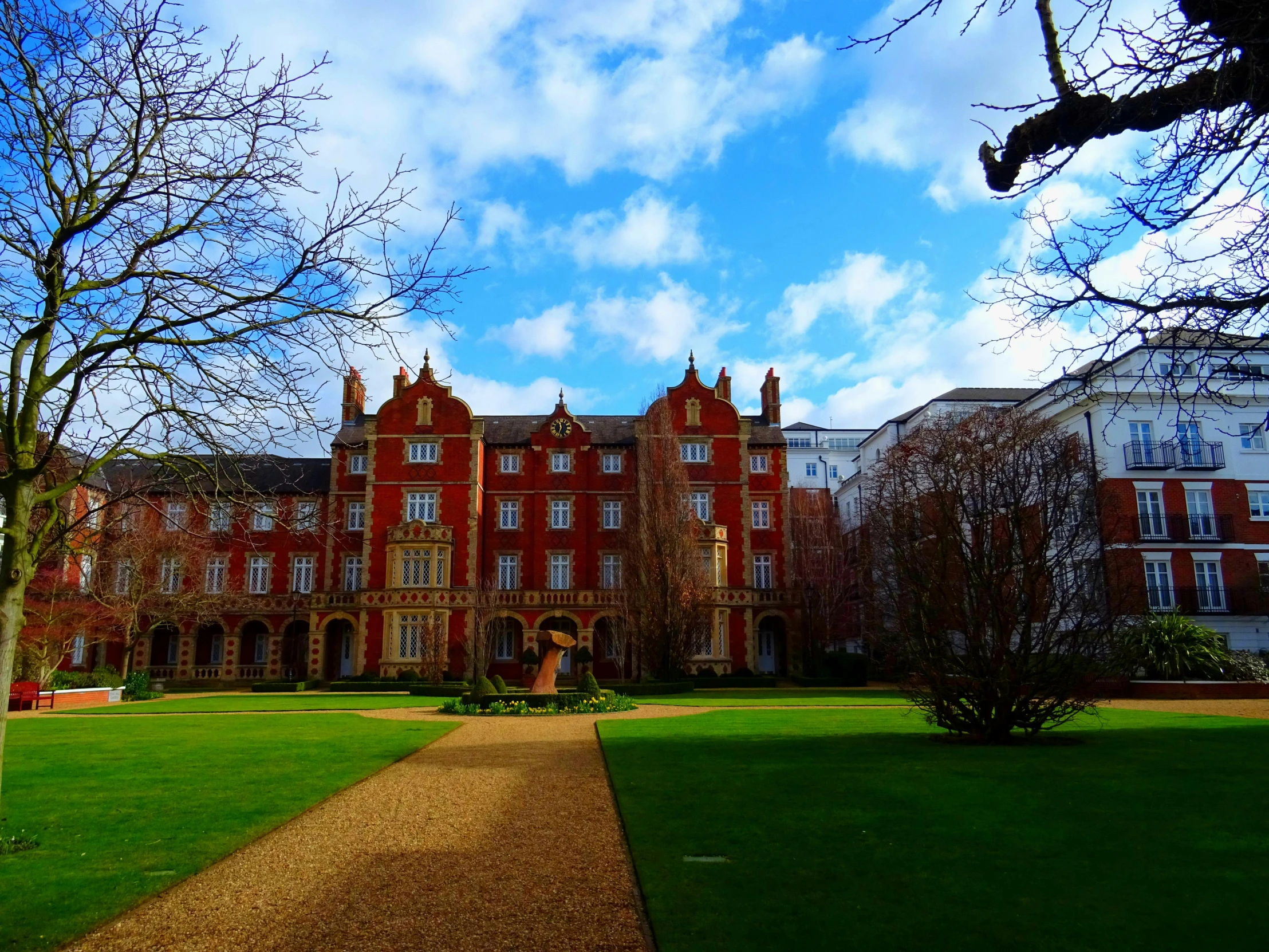 a large red brick building sitting on top of a lush green field, inspired by Samuel Prout, unsplash, academic art, neo - gothic architecture, courtyard walkway, winter, ralph horley