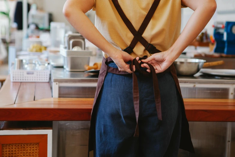 a man that is standing in a kitchen, trending on pexels, suspenders, showing her shoulder from back, wearing an apron, on a wooden table