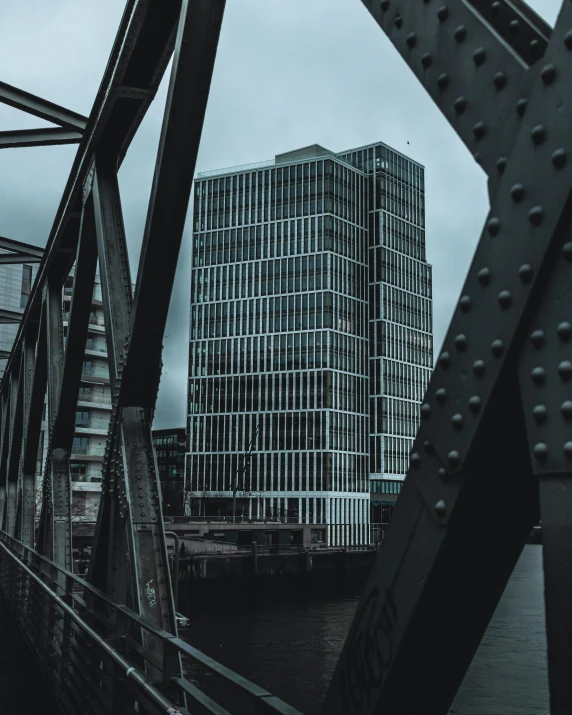 a bridge over a body of water with a building in the background, by Oskar Lüthy, pexels contest winner, brutalism, glasgow, thumbnail, tall building, confident looking
