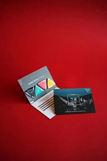 a business card sitting on top of a red surface, a picture, black and teal paper, triangular elements, package cover, kinemacolor